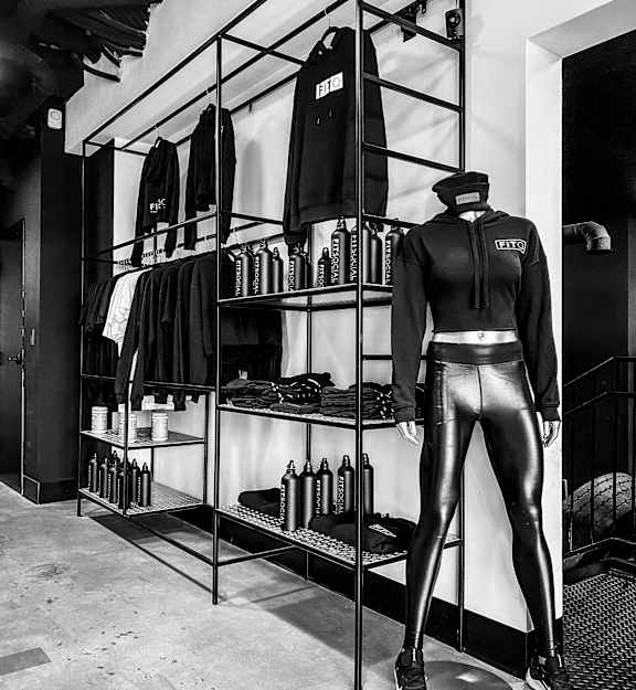 A mannequin stands in front of a clothing rack in a room.