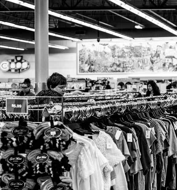 A clothing store with racks of clothes and a woman shopping.