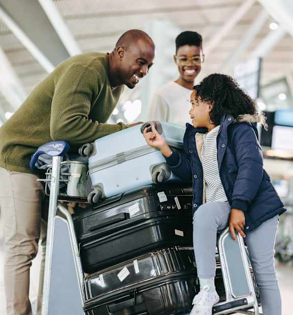 A man and a young girl are standing next to a luggage cart in an airport.