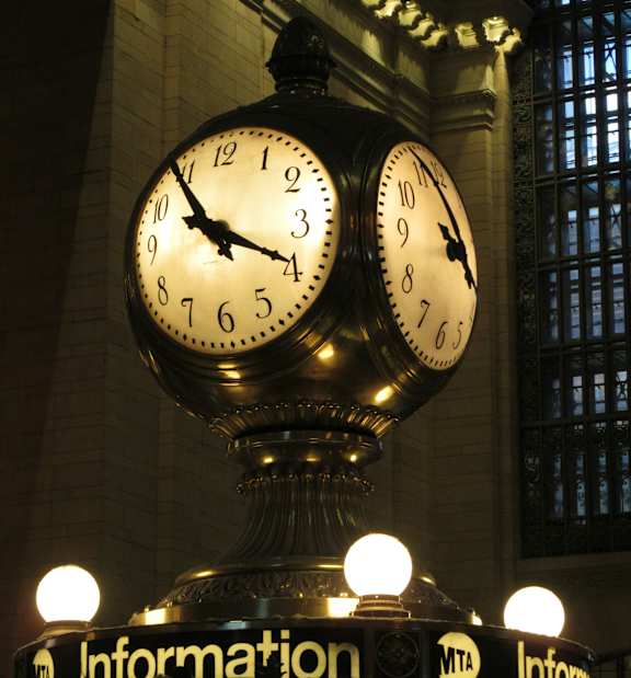 Two clocks on a pole in a train station.