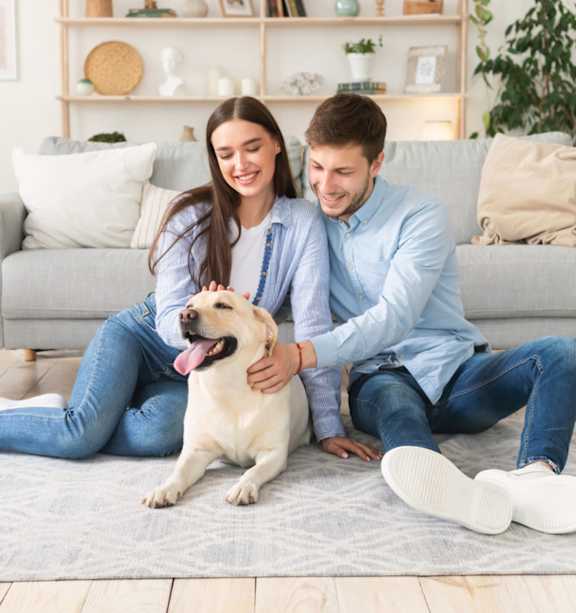 A man and woman sitting on the floor with a dog.