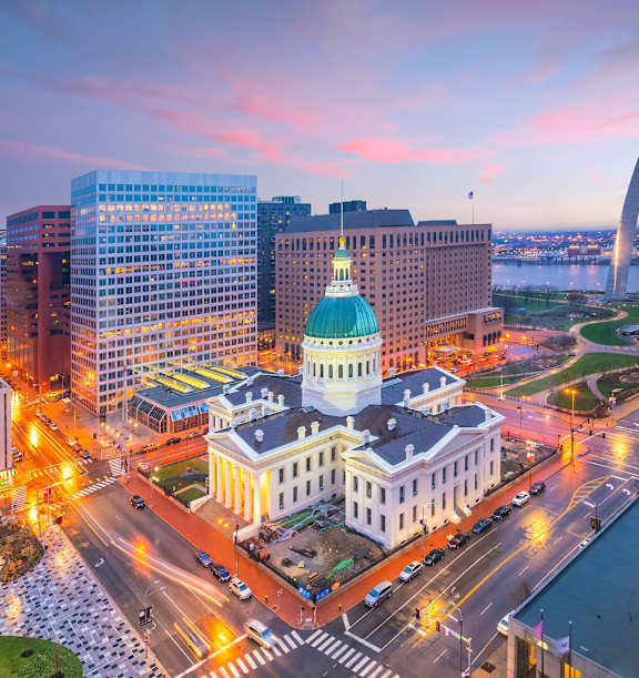 A cityscape with a large white building in the center and a tall arch in the background.