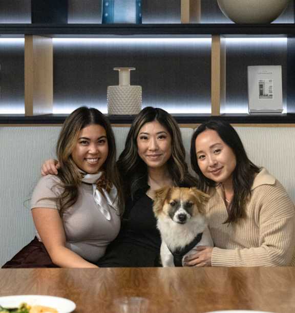 Three women and a dog are sitting at a table.