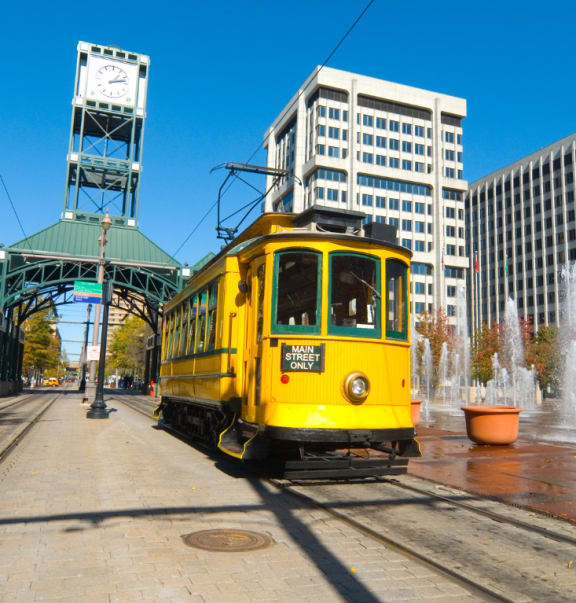 a yellow streetcar is on the tracks in front of a fountain