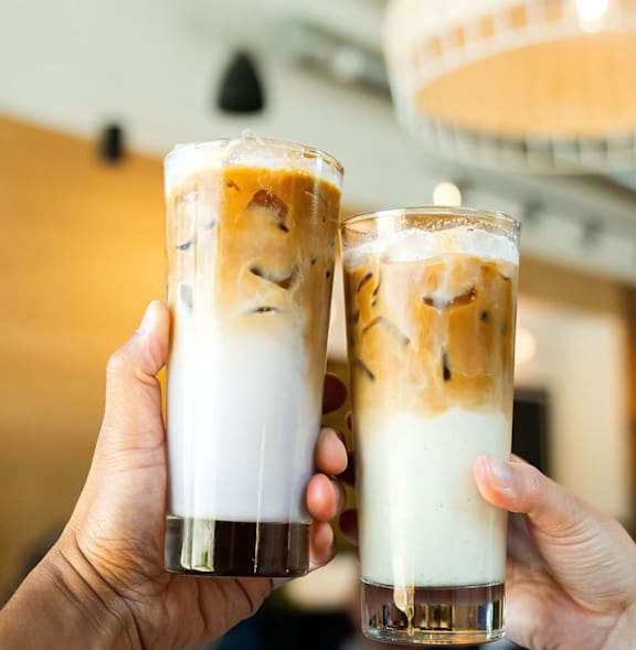 Two hands holding glasses of iced coffee with milk.