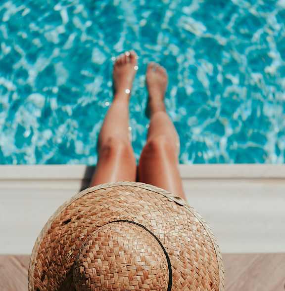 A person wearing a straw hat is sitting by a pool.