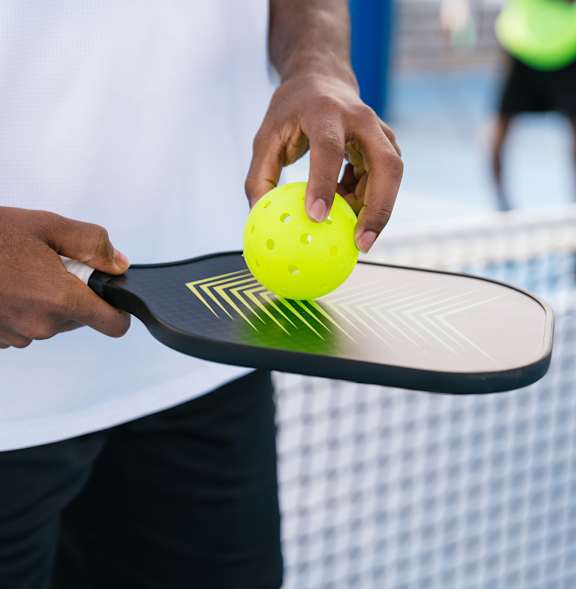 A person holding a tennis racket and ball on a tennis court at Montage at Hawk Ridge Apartments, Missouri