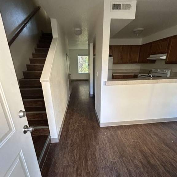 a white door is on the left of a hallway with wooden floors and a staircase.
