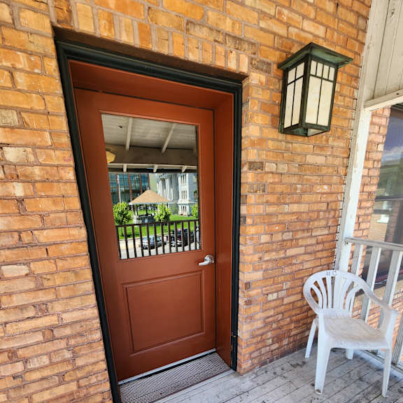 a window with a brown wooden door and a white chair on the wall.