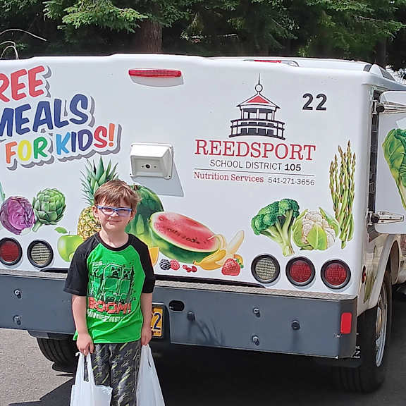 a truck with a reedsport school district logo and a sign that says "free meals for kids!" is parked in a parking lot.