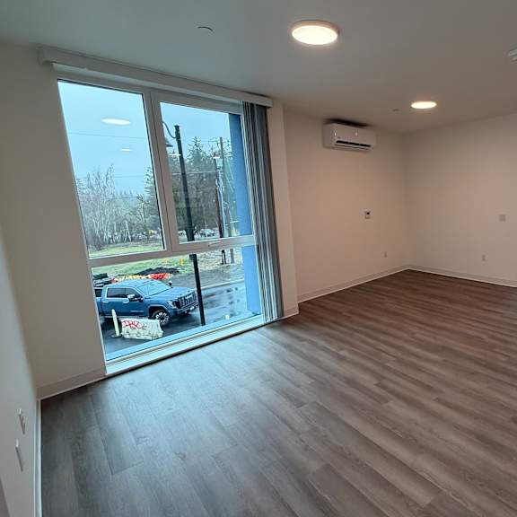 a spacious room with wooden flooring and a kitchen area in the background.