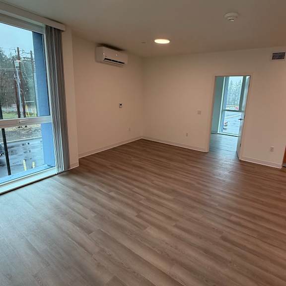 a spacious room with wooden flooring and a kitchen area in the background.