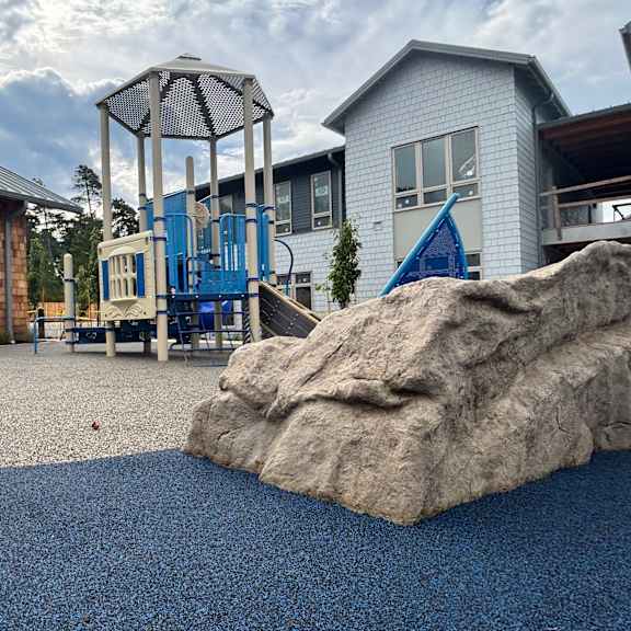 a playground with a large rock in the foreground and a swing set in the background.