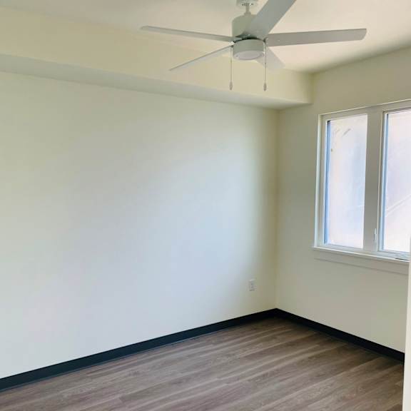 an empty room with a ceiling fan and two windows