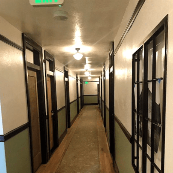 a long hallway with doors on the left and windows on the right.