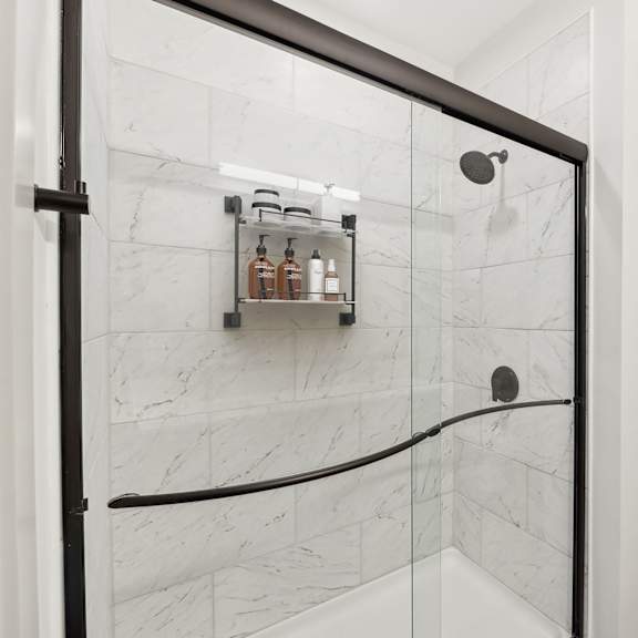 Thumbnail 13 of 21 A bathroom with a marble wall and a shelf with bottles on it.