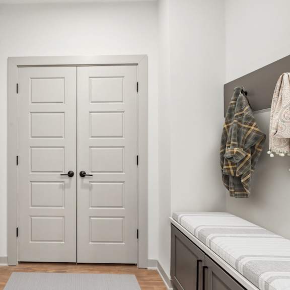 Thumbnail 5 of 21 A white door is in a hallway with a bench and coat rack.