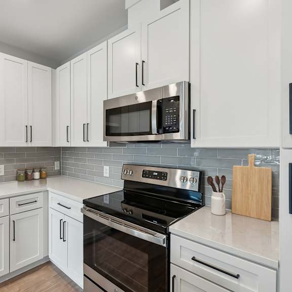 Thumbnail 4 of 21 A kitchen with white cabinets and a black stove top oven.