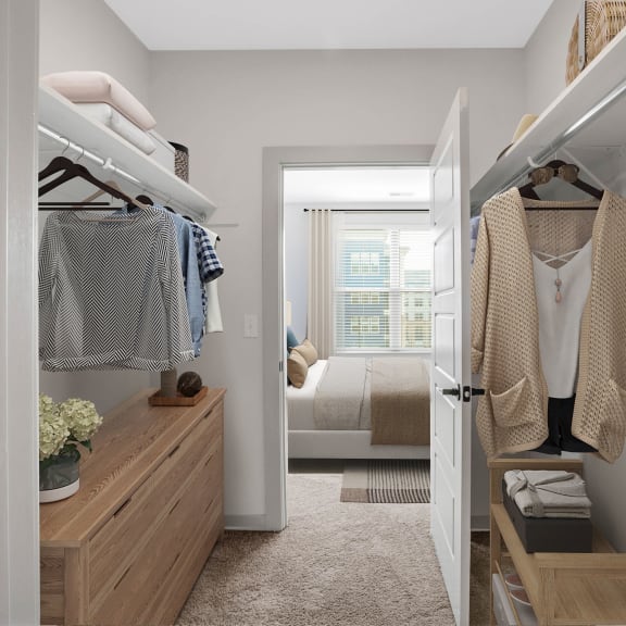 Thumbnail 8 of 12 a walk in closet with clothes hanging on a rack and a bedroom in the background