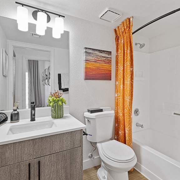 A bathroom with a white toilet, sink, and orange shower curtain.