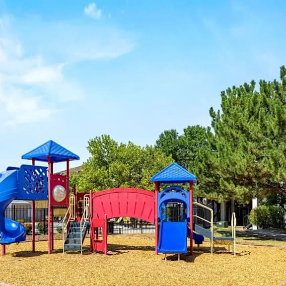 A playground with a blue slide, red slide, and a blue and red playhouse.