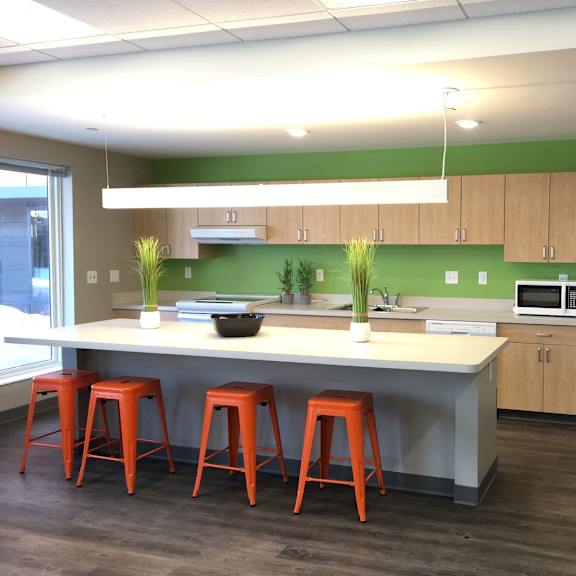 a kitchen with a white refrigerator, orange stools, and a white counter.