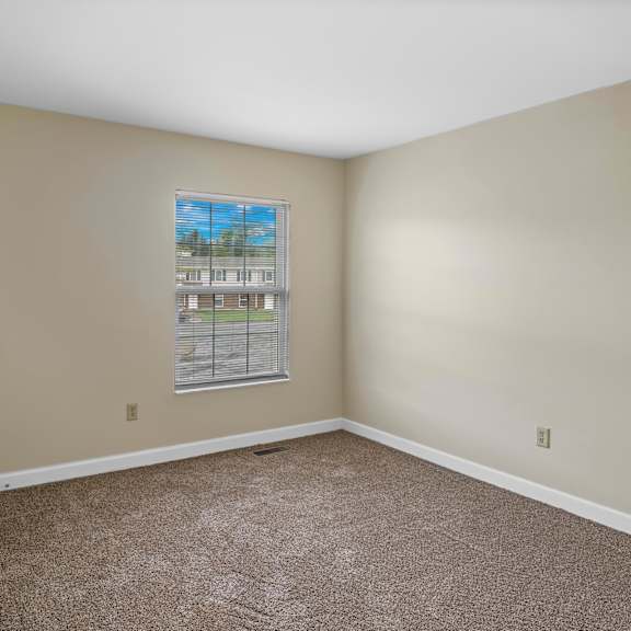 a room with a carpeted floor and a window showing a view of a building.