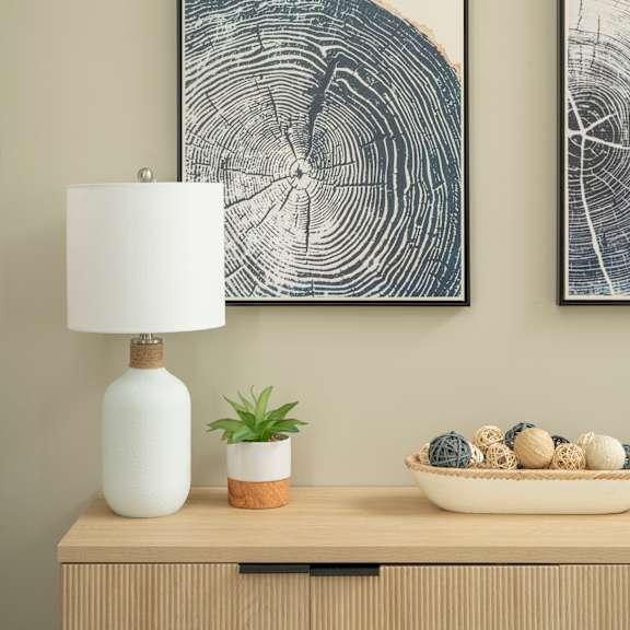 A table with a white lamp, a plant, and a bowl of decorative balls.