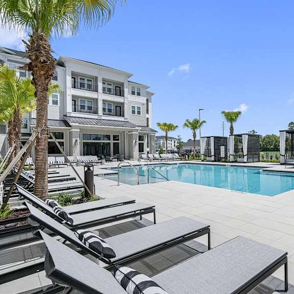 a swimming pool with lounge chairs and a building in the background at madison waterford lakes, orlando, 32826