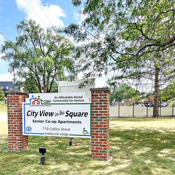 a sign for city view in the square senior co-op apartments stands in a grassy area.