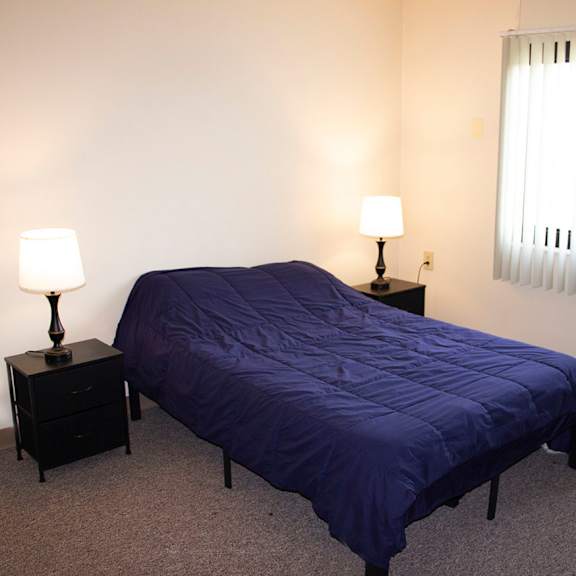 a bedroom with a bed, two nightstands with lamps, and a window with blinds.