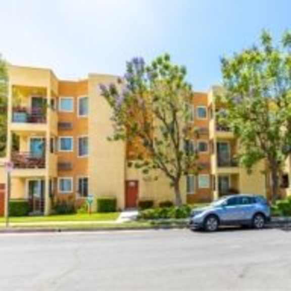 a parking lot in front of a multi-story apartment building with cars parked.