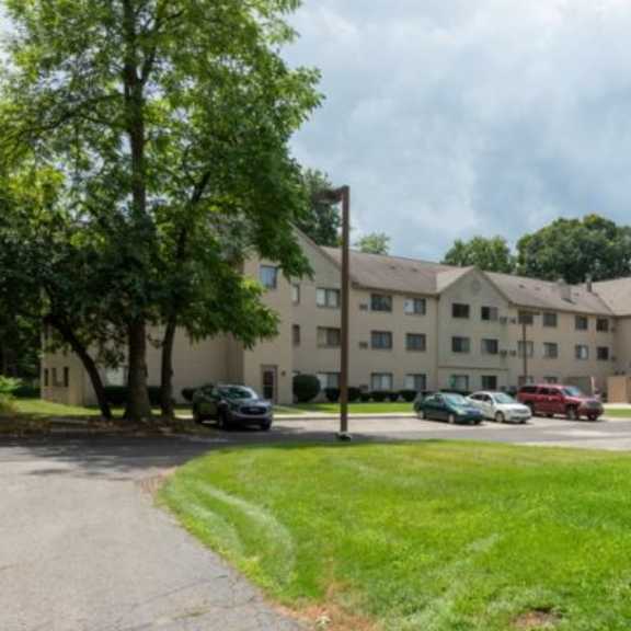a large apartment complex with a grassy area in front and cars parked in the driveway.