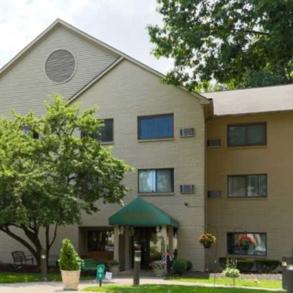 a beige building with a green roof and a tree in front.