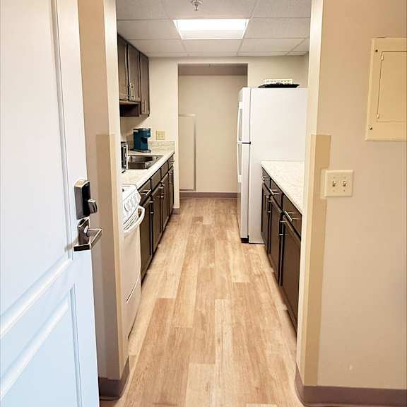 a white door is open to a kitchen with wooden floors.