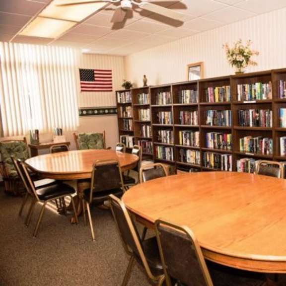 a library with a round table and chairs in the foreground and bookshelves filled with books in the background.