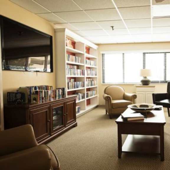 a living room with a brown couch, a coffee table, and a bookshelf filled with books.