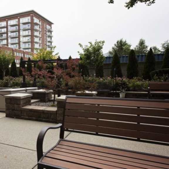 a brown bench sits in a courtyard with a building in the background.