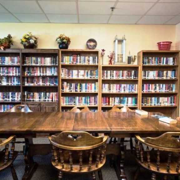 a library with a long table and chairs in front of bookshelves.