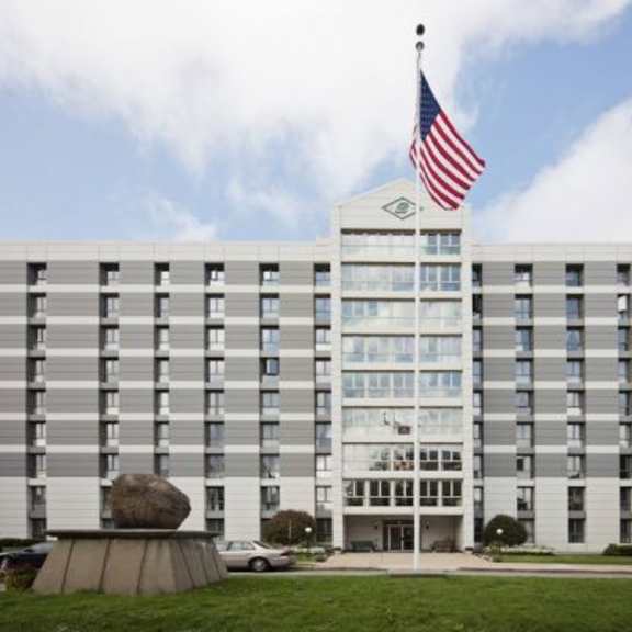 a large building with a flag on top and a stone monument in front.