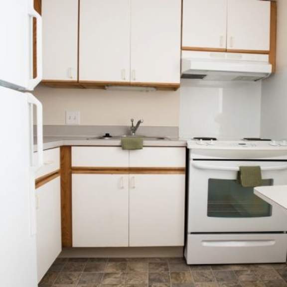 a white refrigerator is on the left in a kitchen with white cabinets and a white stove.