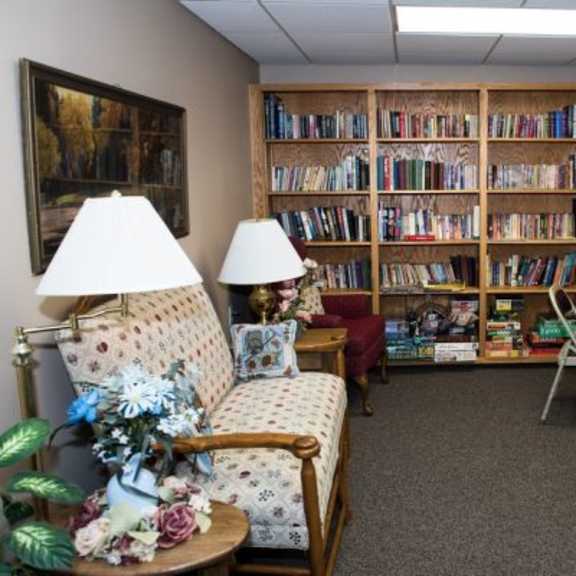 a room with a large bookshelf filled with books, a table with chairs, and a vintage chair with a floral pattern.