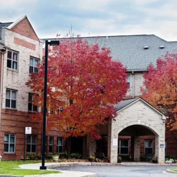 a red brick building with a flag on top and trees with red leaves in front.