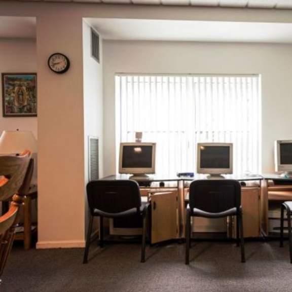 three computers are on a desk in a room with a clock on the wall.