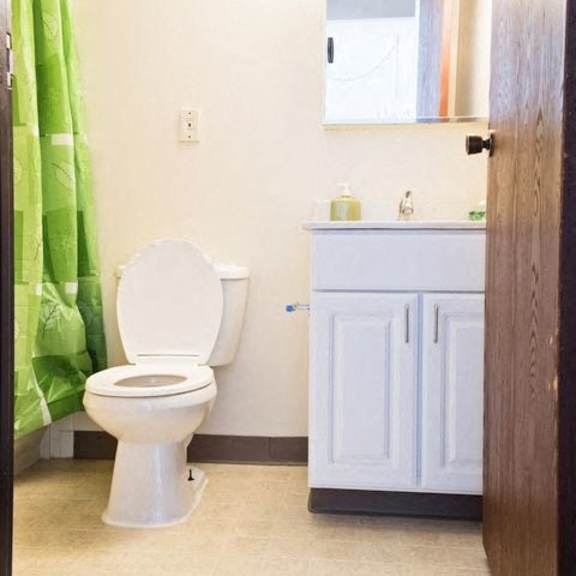a white toilet in a bathroom with a green shower curtain.
