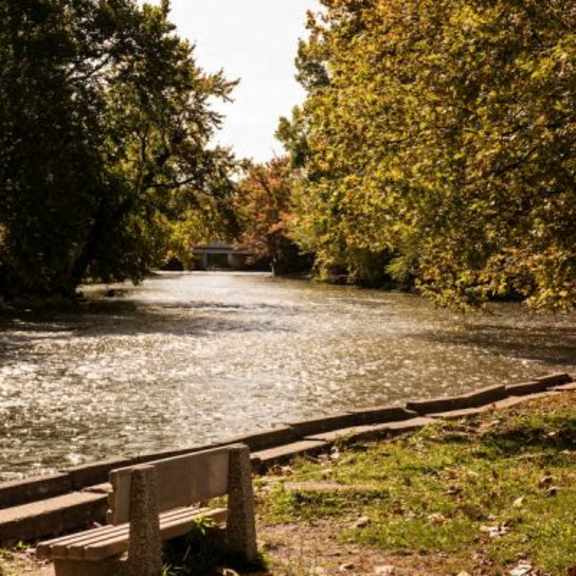a bench sits on the grass next to a river.