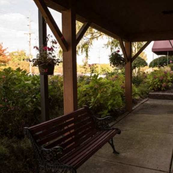 a wooden bench sits under a covered patio area.