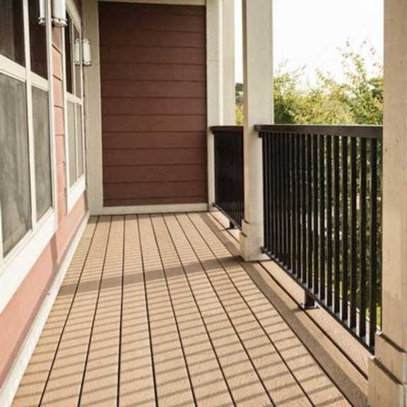 a wooden porch with a black railing and a brown door.