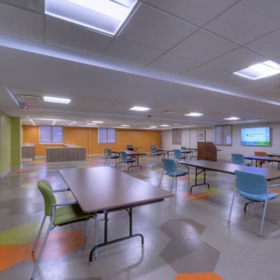 a room with tables and chairs and a tv on the wall.