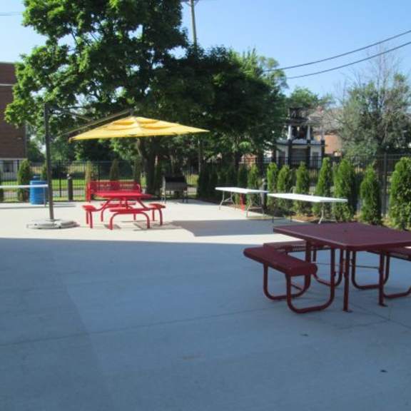 a red picnic table is in the middle of a concrete area with a yellow umbrella and red chairs.